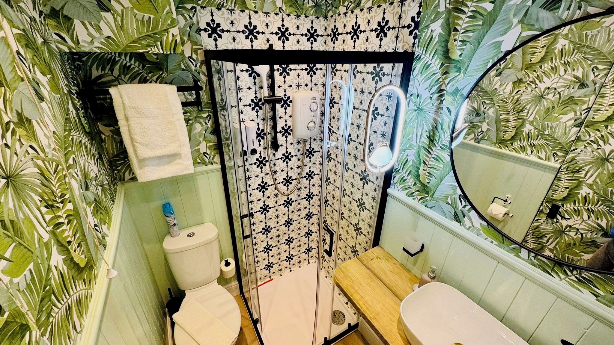 A bathroom with a toilet, sink, shower, and a mirror.
