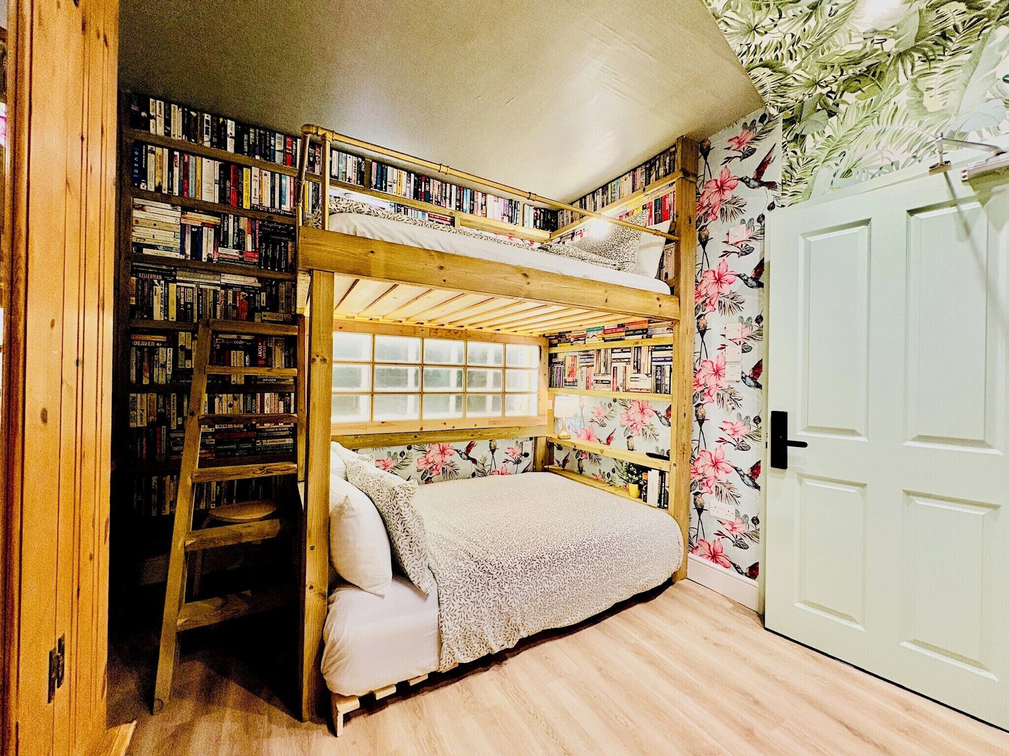 Een stapelbed met houten frame, een ladder en een raam. Aan beide kanten van het bed staan boekenkasten.