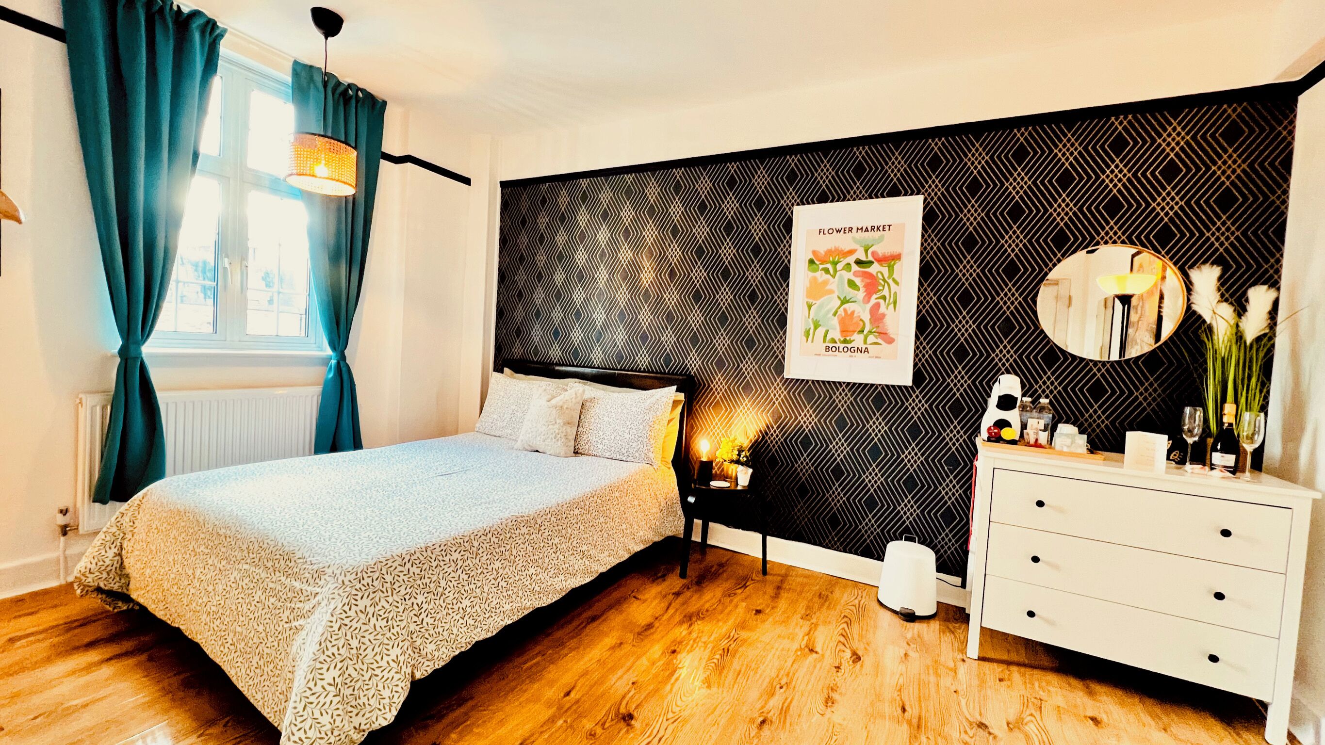 A bedroom with a bed, a dresser, a nightstand, a wall with a geometric pattern, and a poster.