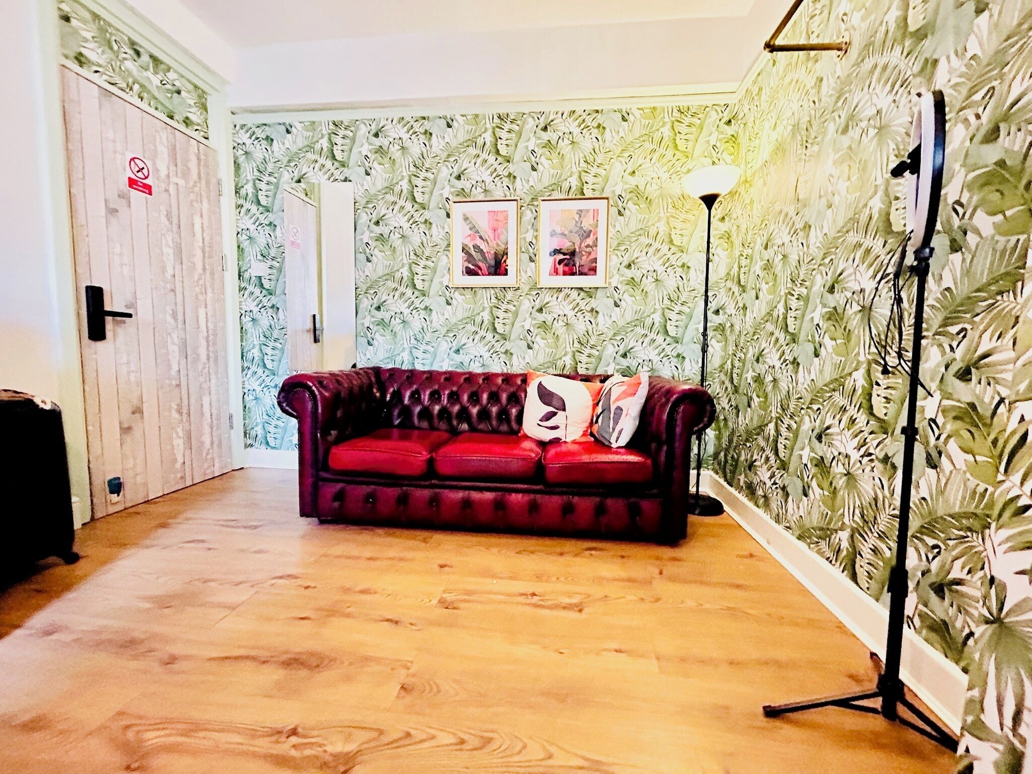 A room with a red sofa, wooden flooring, a door with a 'No Entry' sign, and a wall with a leafy pattern.