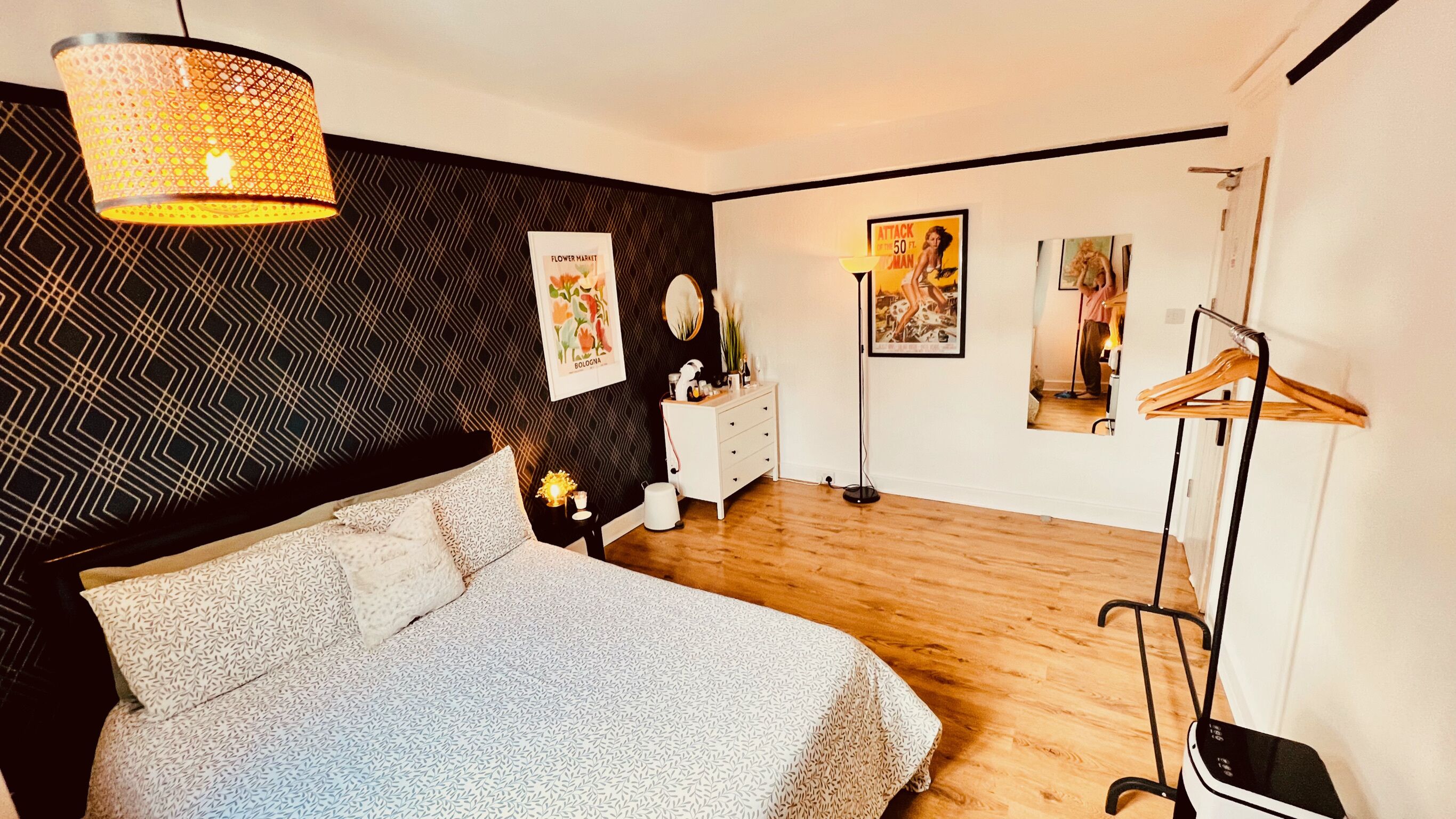 A modern bedroom with a patterned bedspread, a hanging light fixture, a dresser, and artwork on the walls.