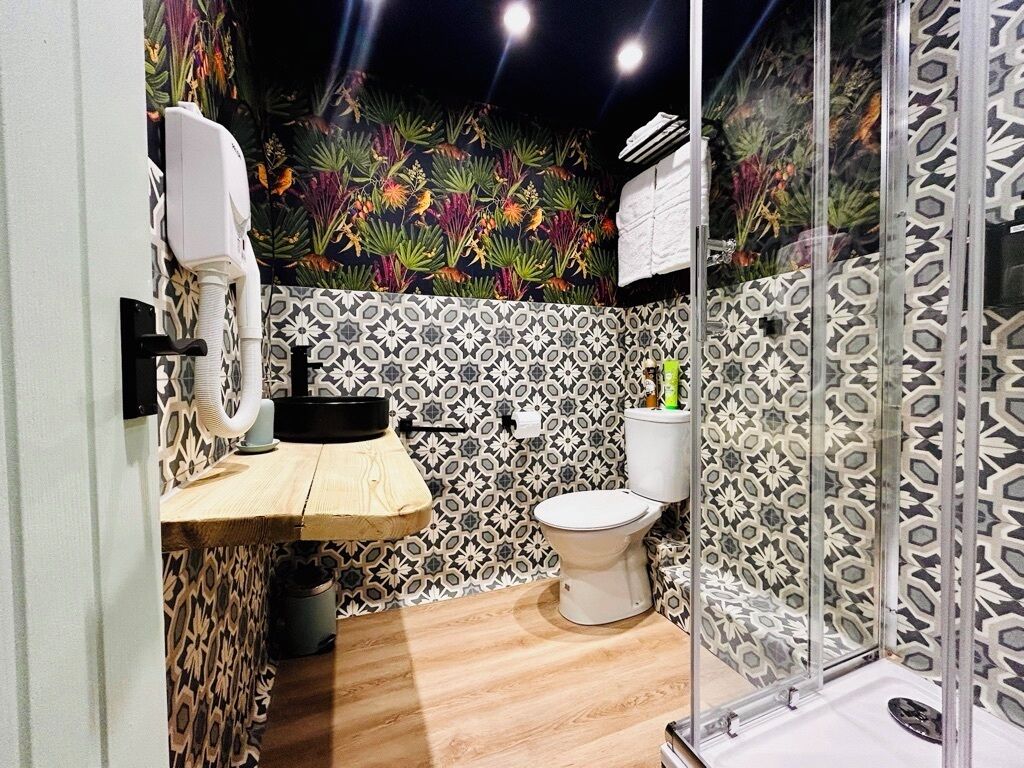 A bathroom with a patterned wall, a toilet, a shower with a glass door, and a sink with a hanging towel rack.