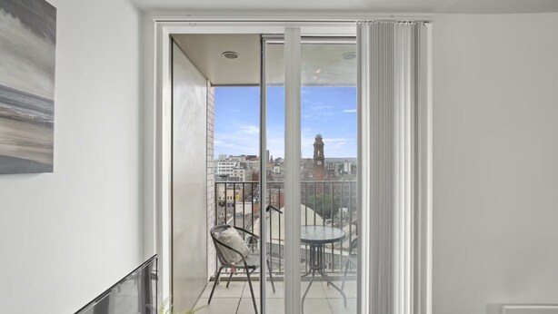 Ein Balkon mit Glasdoor, einem Stuhl, einem kleinen Tisch und Blick auf die Stadtlandschaft.