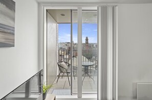 Un balcón con puerta de cristal, una silla, una mesita y vista panorámica de la ciudad.