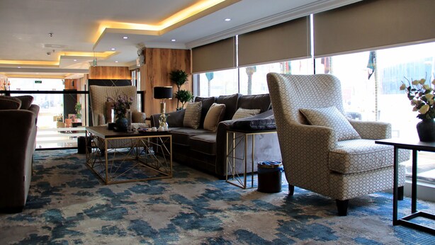 A spacious living area with a sofa, armchair, and coffee table, large windows, and a patterned carpet. - Swat Serviced Apartments 4 (Al Khobar)
