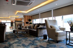 A spacious living area with a sofa, armchair, and coffee table, large windows, and a patterned carpet.