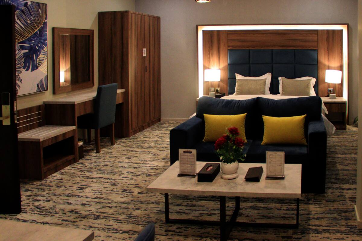 A hotel room with a large bed, a desk, a chair, and a coffee table with a vase of flowers.
