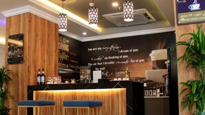 A coffee shop interior with a wooden counter, bar stools, hanging pendant lights, and a wall with a coffee-related quote. - Swat Serviced Apartments 4 (Al Khobar)