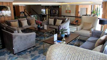 A spacious lobby with multiple seating areas, a reception desk, and a staircase leading to upper floors.
