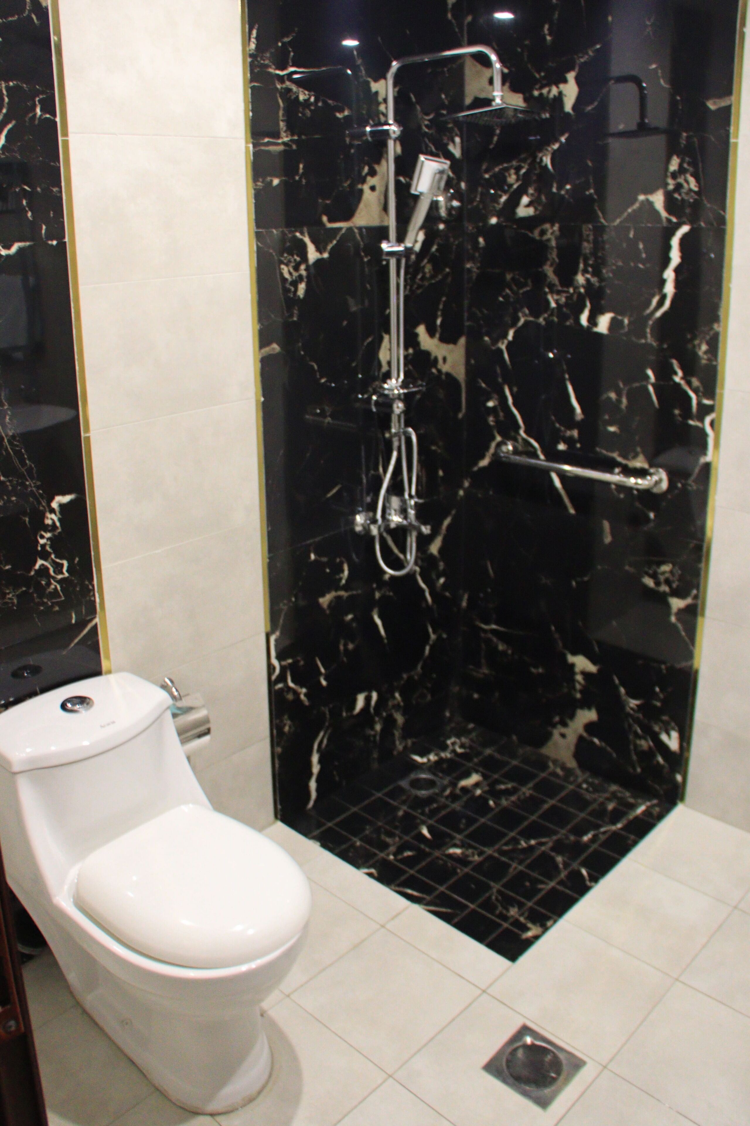 Un baño con inodoro blanco, cabina de ducha con revestimiento de mármol blanco y negro, y suelo de baldosas.