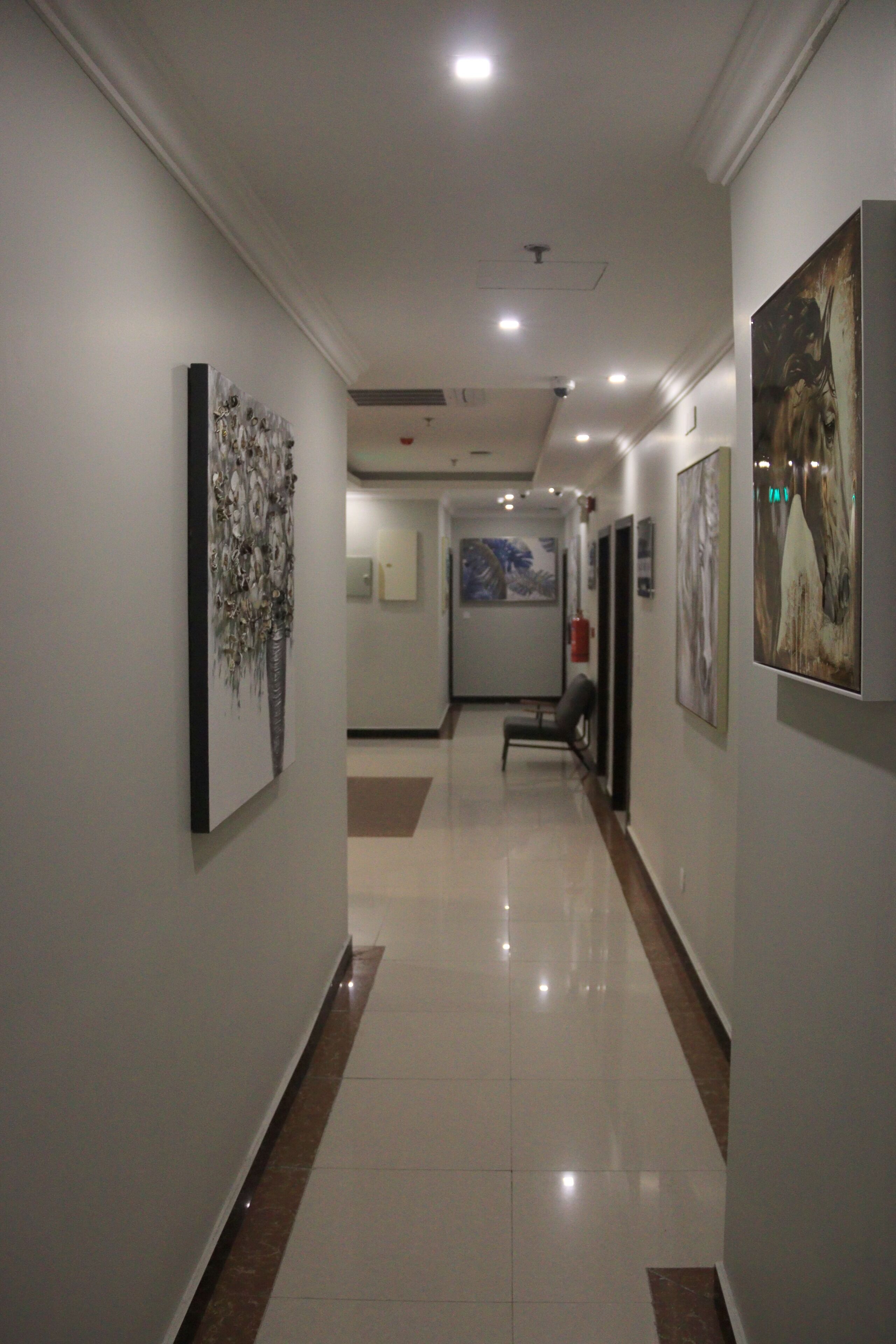 A hallway with artwork on the walls, a chair, and a fire extinguisher.