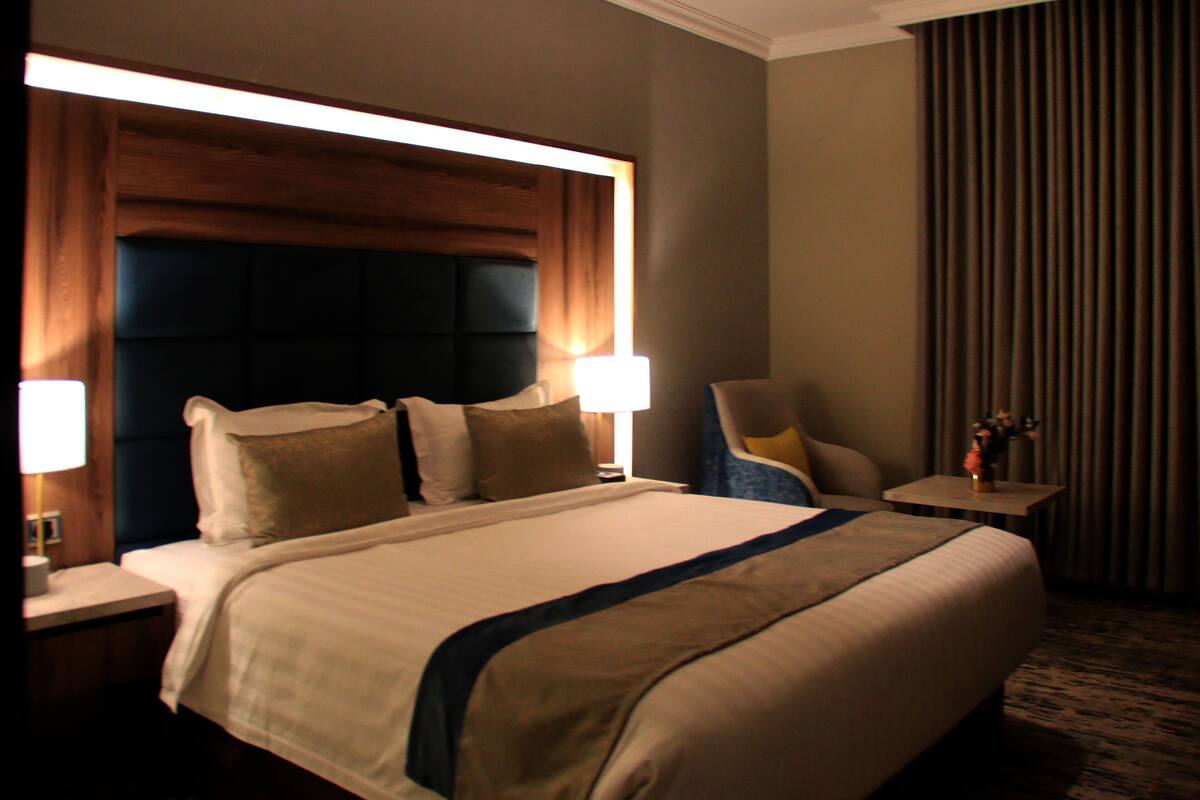 A hotel room with a large bed, two bedside tables, a chair, a lamp, and a curtain.