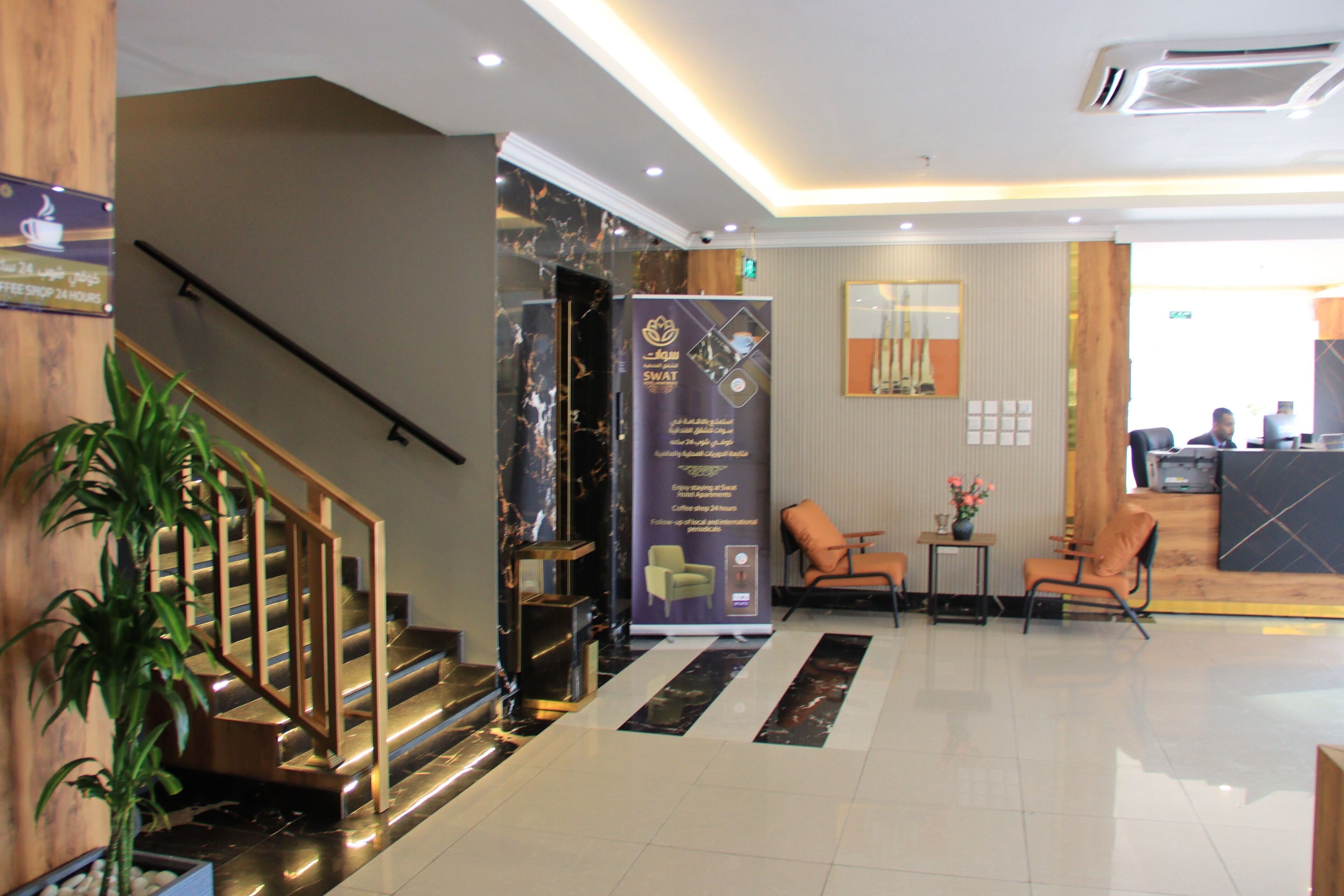 A hotel lobby with a reception desk, seating area, and a staircase.