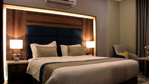 A hotel room with a large bed, two bedside lamps, a wooden headboard, and a small table with a chair. - Swat Serviced Apartments 4 (Al Khobar)