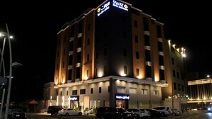 A multi-story hotel with illuminated signage, a parking lot with several cars, and a well-lit facade. - Swat Serviced Apartments 4 (Al Khobar)