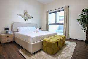 A modern bedroom with a bed, bedside tables, a window with curtains, and a potted plant. - Stylish 1BR in Azizi Iris, Al Furjan (Dubai)