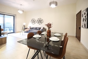 A dining area with a glass table, brown chairs, and a vase with dried plants. - Stylish 1BR in Azizi Iris, Al Furjan (Dubai)