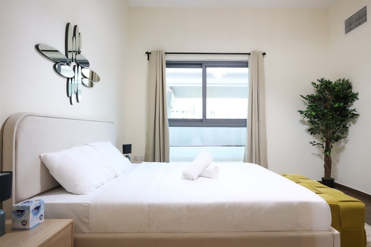 Une chambre d’hôtel avec un lit, une table de chevet, un miroir, une fenêtre avec des rideaux et une plante en pot.