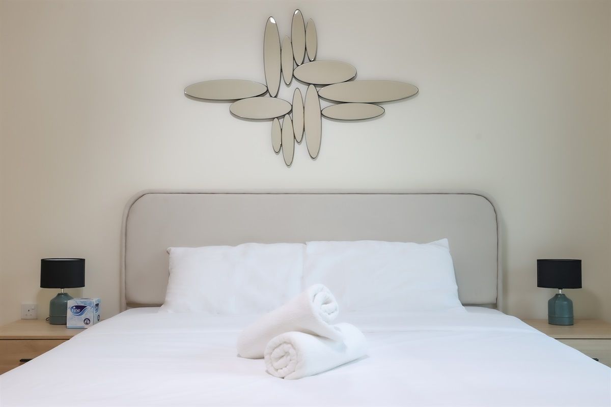 Een hotelkamer met een opgemaakt bed, twee nachtkastjes met lampen, en een decoratief object aan de muur.