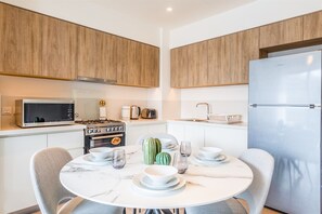 A modern kitchen with wooden cabinets, a stainless steel refrigerator, a microwave, a stove, and a dining table set for four. - Upscale & Stylish 2BR Dubai Hills (Dubai)