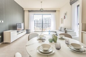 Ein modernes Wohnzimmer mit Essbereich, einer Sofagarnitur und Blick auf die Stadtlandschaft.
