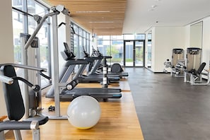 A gym with exercise equipment, a large window, and a wooden floor. - Upscale & Stylish 2BR Dubai Hills (Dubai)