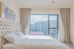 A hotel room with a large bed, a tufted headboard, a large window with curtains, and framed artwork on the wall. - Upscale & Stylish 2BR Dubai Hills (Dubai)