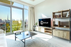 A modern living room with a large window, a flat-screen TV, a bookshelf, and a sofa. - Skyline Oasis 1 BR Burj Khalifa Downtown View (Dubai)