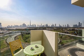 A balcony with a table and chair, overlooking a city skyline with a highway and greenery. - Skyline Oasis 1 BR Burj Khalifa Downtown View (Dubai)