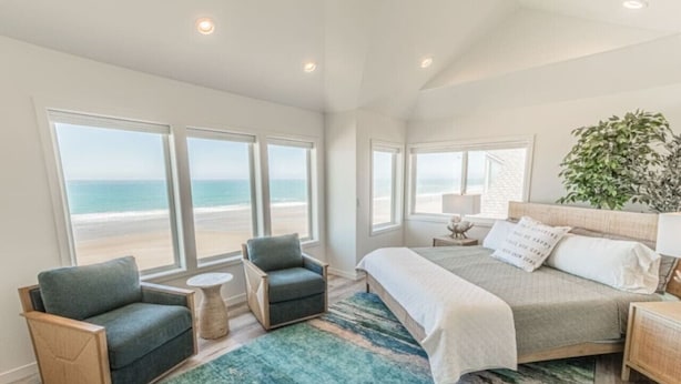 A bedroom with a large bed, two armchairs, a small table, and a view of the beach. - Beach Me! Oceanfront steps2sand (Lincoln City)