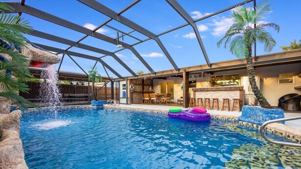 Una piscina interior con caída de agua, rodeada de palmeras y una zona de estar cubierta.