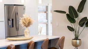 Una cocina moderna con un refrigerador de acero inoxidable, una zona de bar con taburetes de cuero y una planta en maceta.