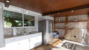 Una cocina moderna con un refrigerador de acero inoxidable, armarios blancos, una encimera de granito y un ventanal grande.