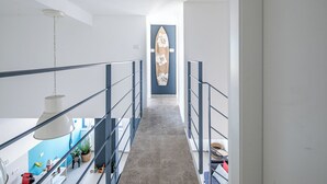 En smal hall med en taklampa, en surfbräda som dekoration på väggen och en trappa med räcken.