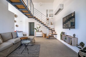 Ein modernes Wohnzimmer mit Treppe, Sofa, Couchtisch und Wand-Fernseher.