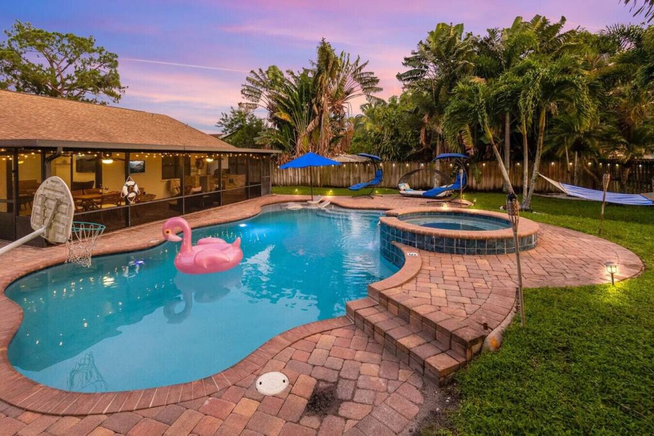 A swimming pool with a pink flamingo float, a hot tub, and a covered seating area with string lights.