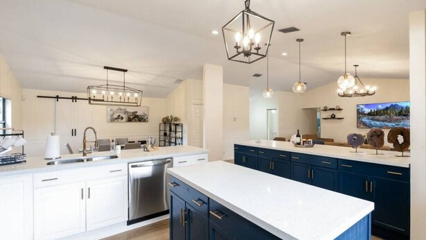 A modern kitchen with white and dark blue cabinetry, stainless steel appliances, and pendant lighting.