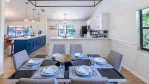 A modern dining area with a glass-top table set for six, surrounded by grey upholstered chairs.