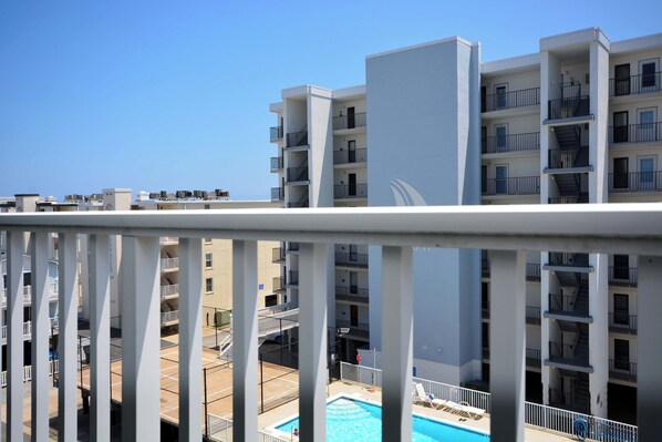 A multi-story hotel with balconies, a swimming pool, and a clear blue sky.