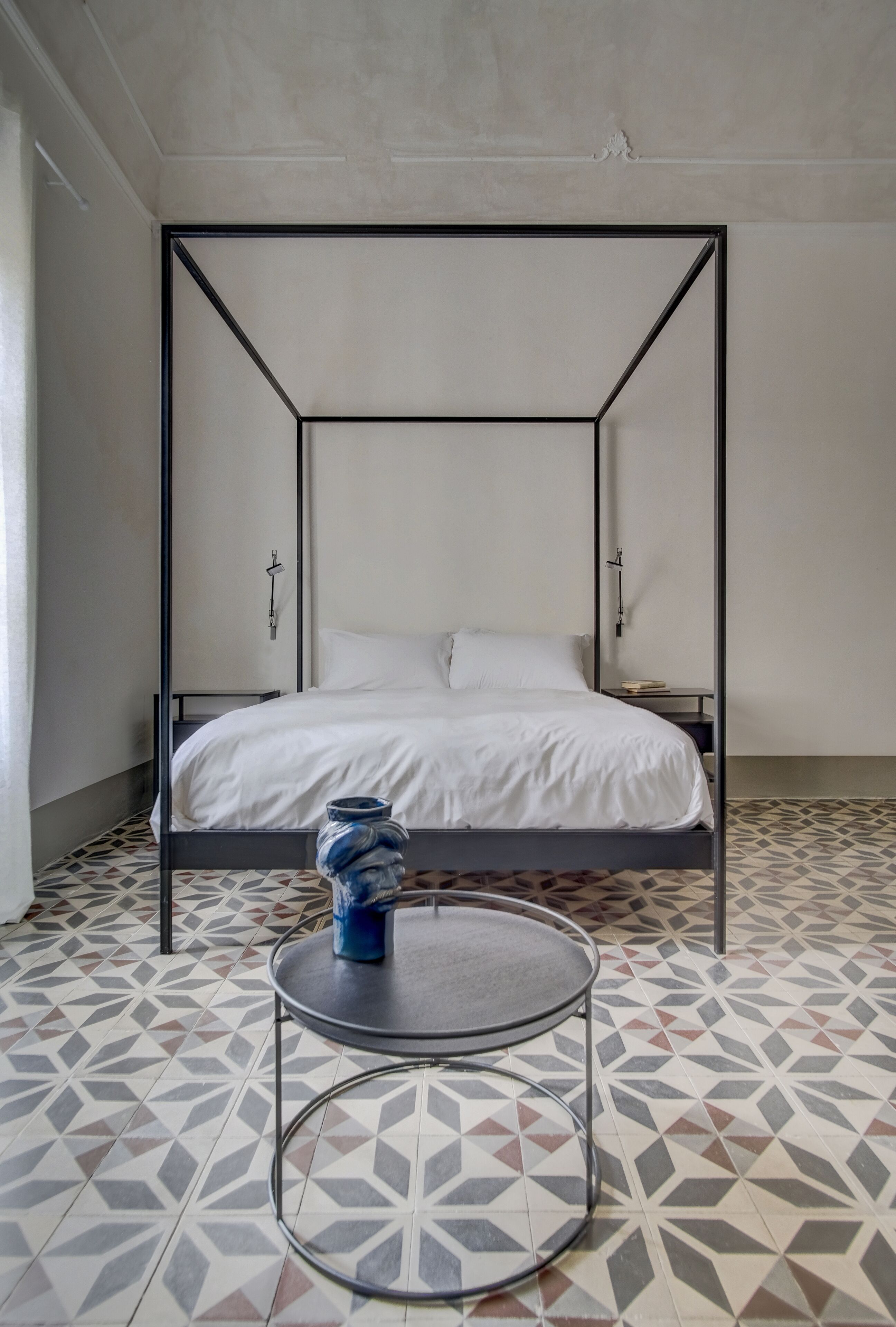 A room with a four-poster bed, a small round table, and patterned floor tiles.