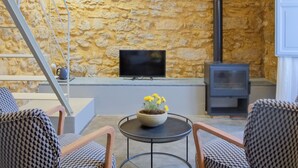 A cozy room with a stone wall, a TV, a fireplace, and two patterned chairs. - Dimora SIQU (Menfi)