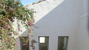 A courtyard with a person walking, a tree with pink flowers, and three windows. - Dimora SIQU (Menfi)