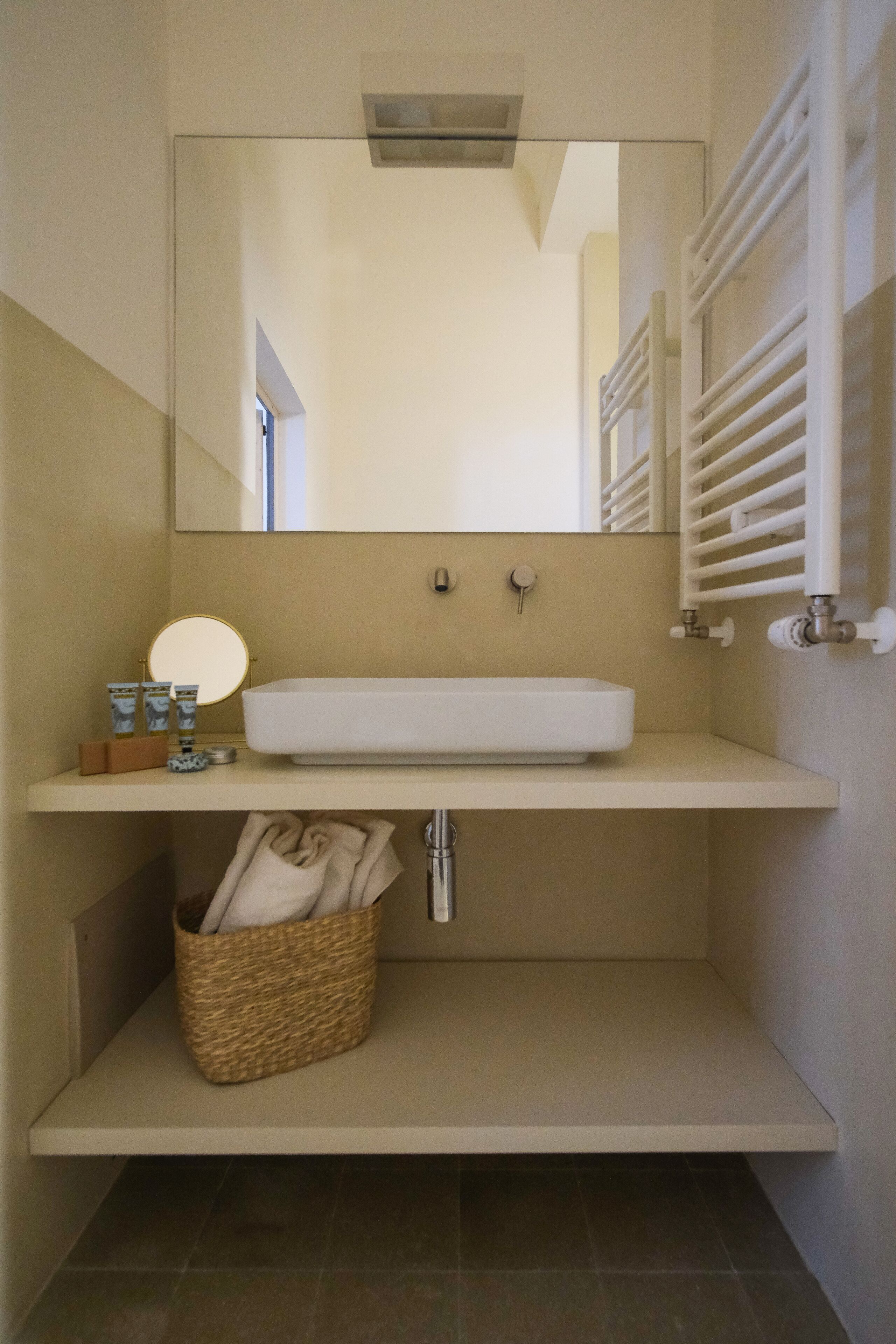 Un baño con un lavamanos blanco, un espejo, un perchero y una cesta debajo del lavamanos.