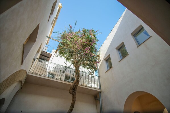 Un patio estrecho con un árbol y un balcón.