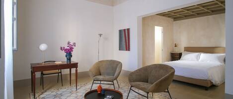 A hotel room with a bed, two armchairs, a small table, a lamp, and a vase with flowers.
