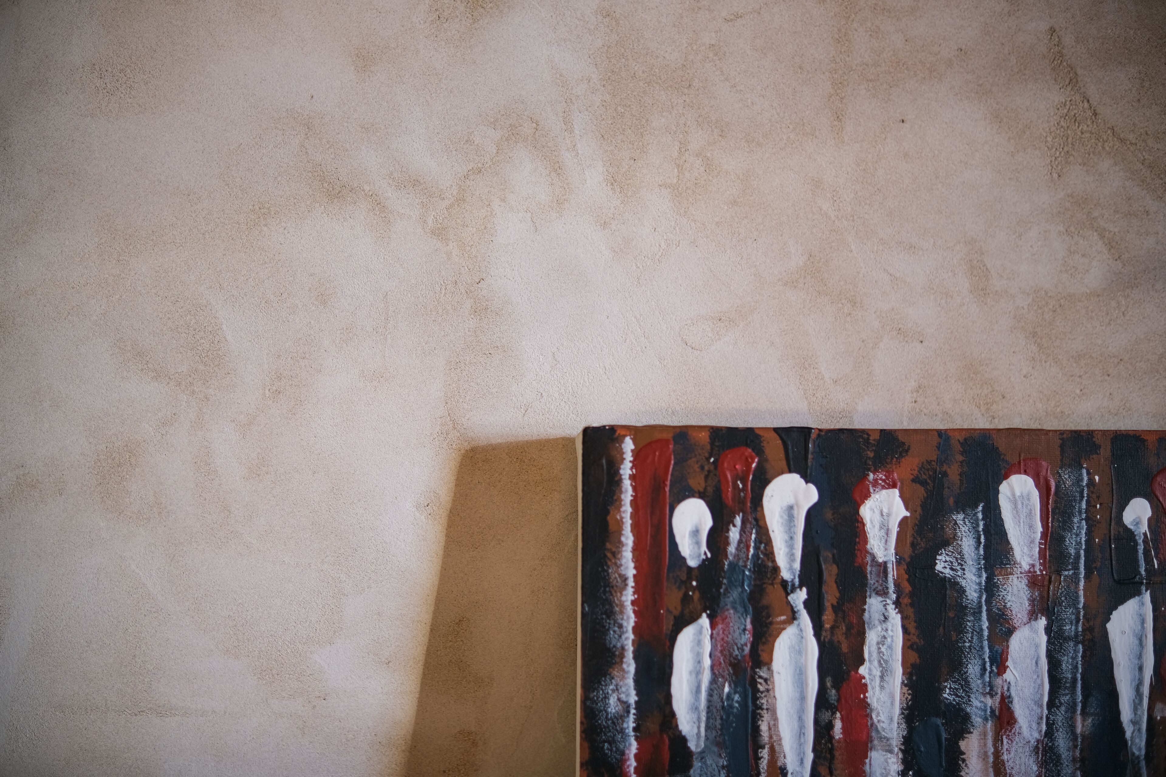 Pared beige con textura y una pintura de figuras abstractas en rojo, blanco y negro.