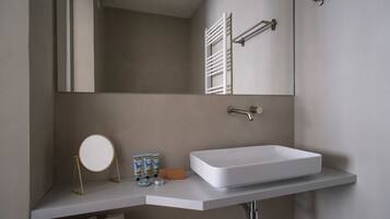 A modern bathroom with a large rectangular sink, a round mirror on a gold stand, and a towel rack above the sink.