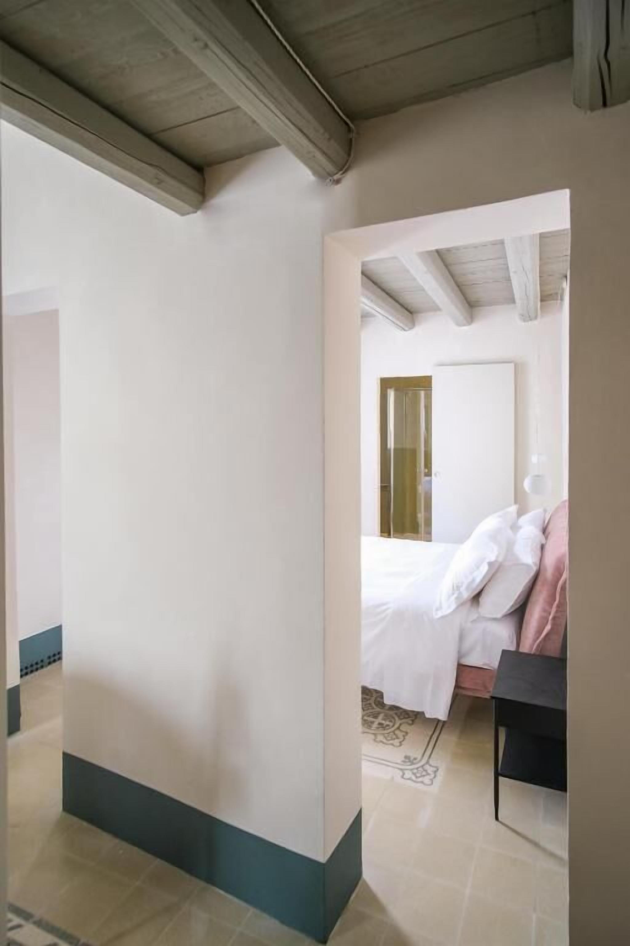 A bedroom with a bed, a nightstand, and a door leading to another room.