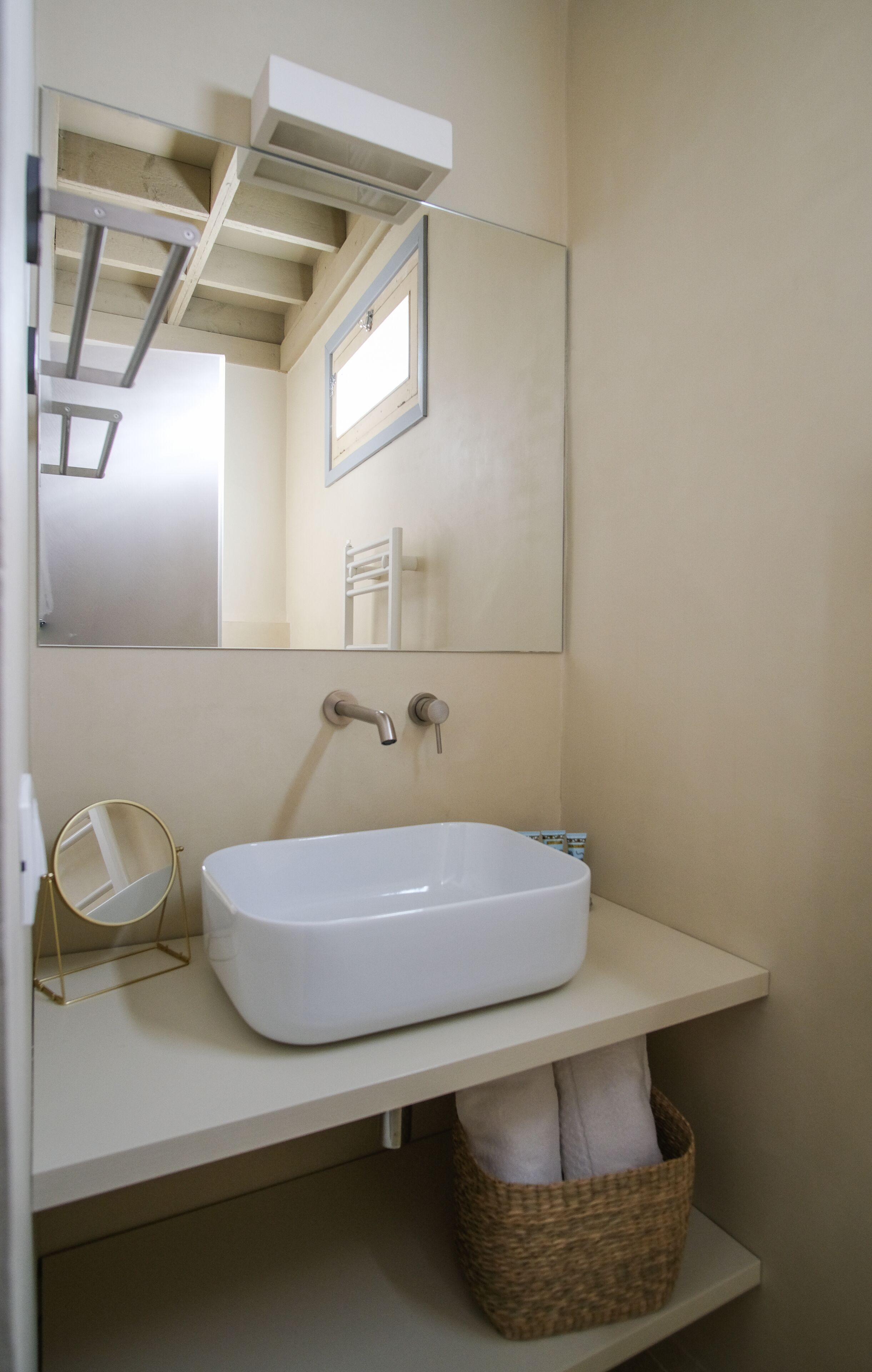 Un bagno con un lavandino bianco, uno specchio e un cesto per gli asciugamani.