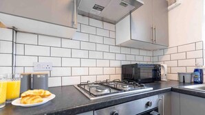 A modern kitchen with white tiles, a gas stove, a microwave, and a sink.